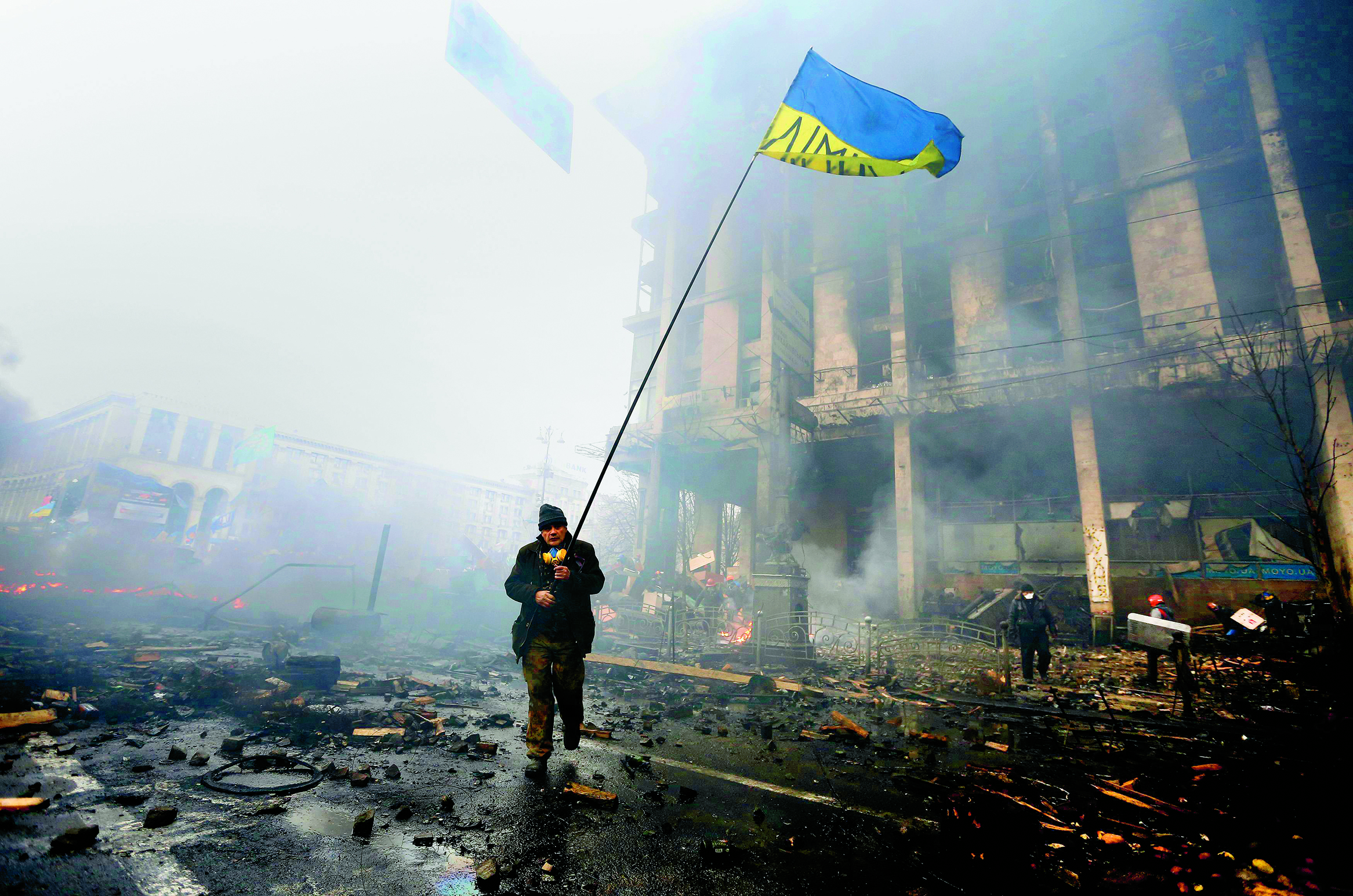 An anti-government protester holds a Ukranian flag as he advances through burning barricades in Kiev